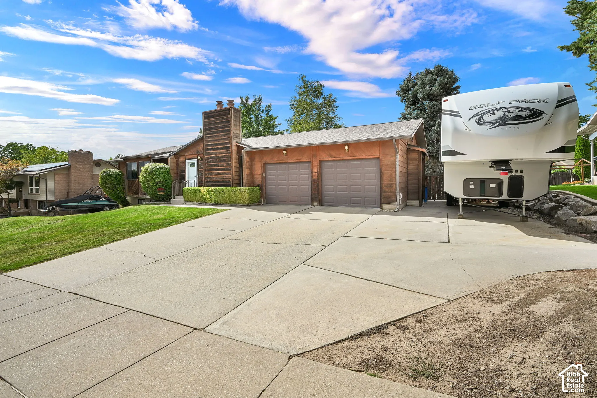 Expansive concrete driveway, attached two-car garage with panel doors, and a wood-paneled exterior