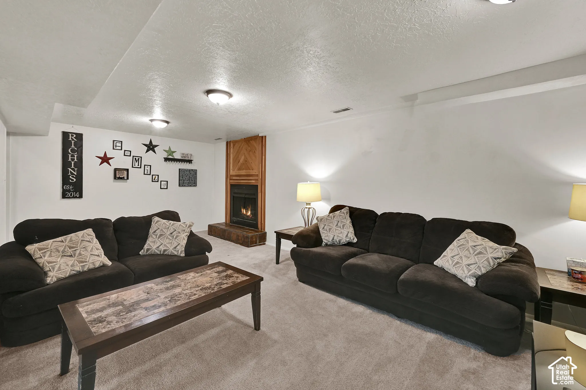 Carpeted living area featuring a fireplace with a wood-paneled surround and hearth, recessed lighting, and white walls