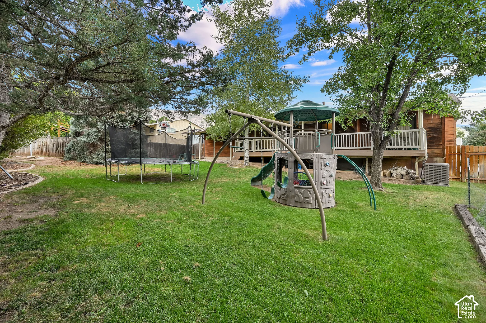 Expansive backyard featuring a lush lawn, mature trees, and a wooden deck with white railings