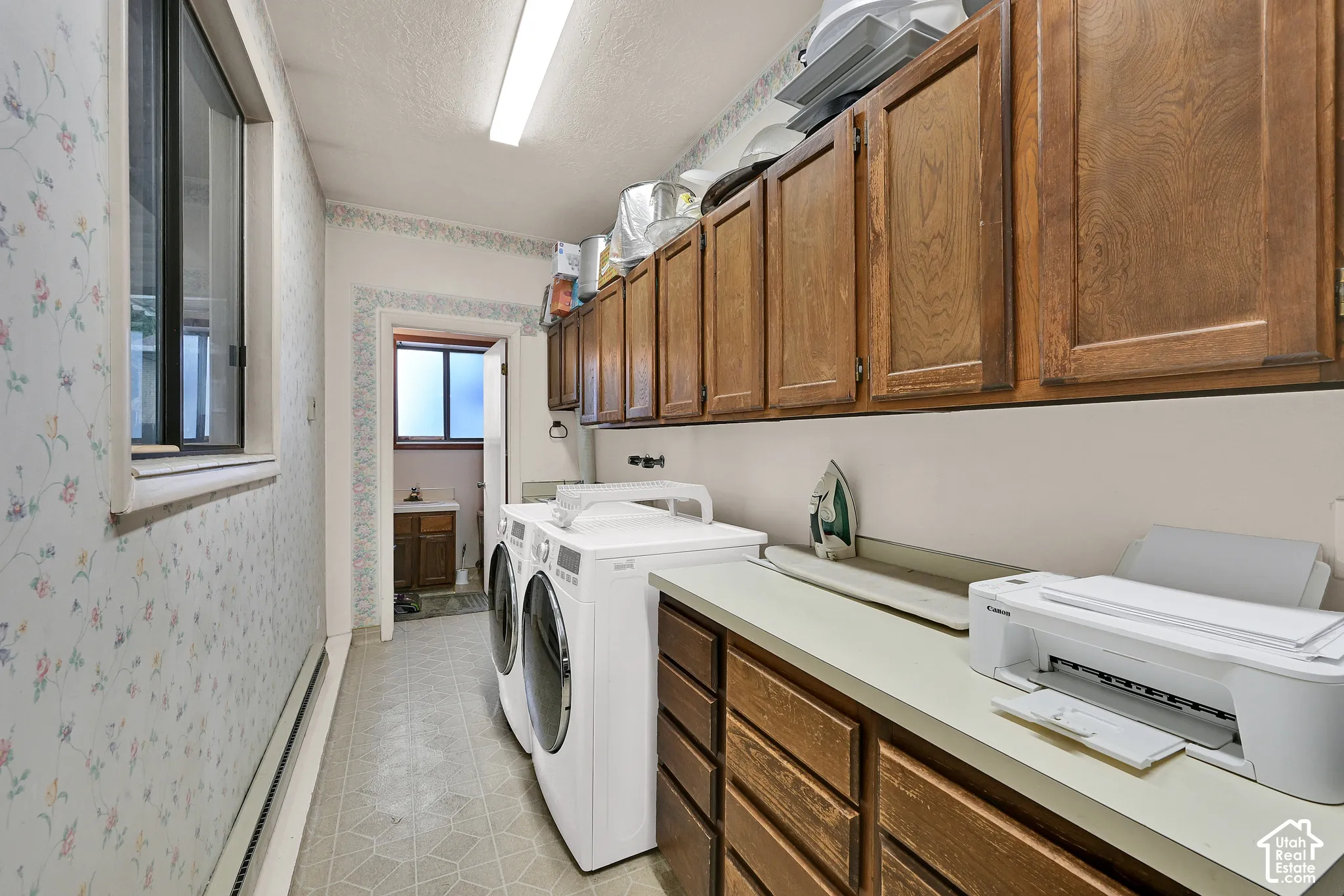 Laundry area with overhead fluorescent lighting, a window, wood-finish cabinetry, and a countertop with integrated sink