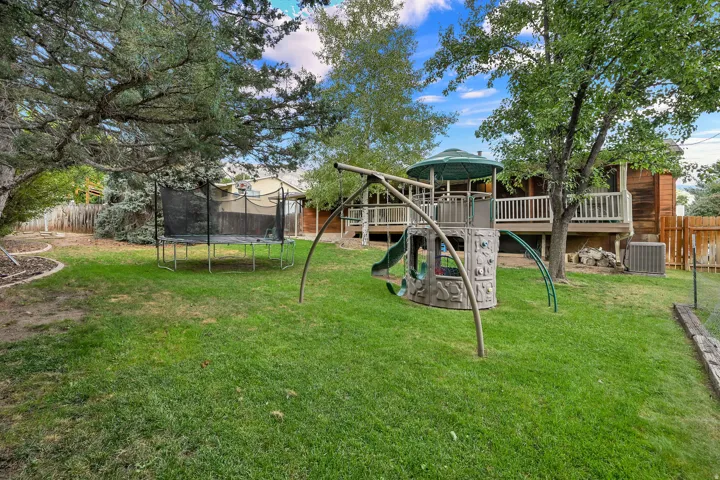 Expansive backyard featuring a lush lawn, mature trees, and a wooden deck with white railings