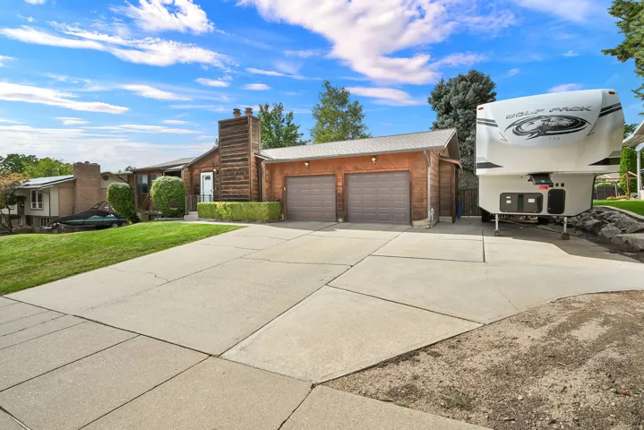 Expansive concrete driveway, attached two-car garage with panel doors, and a wood-paneled exterior