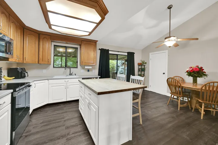 Kitchen featuring wood-finish flooring, white cabinetry, a central island, a vaulted ceiling, and sliding glass doors