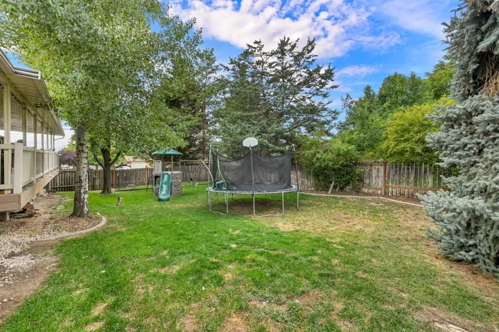 Expansive backyard featuring a manicured lawn, established trees, and a privacy fence