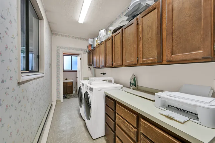 Laundry area with overhead fluorescent lighting, a window, wood-finish cabinetry, and a countertop with integrated sink