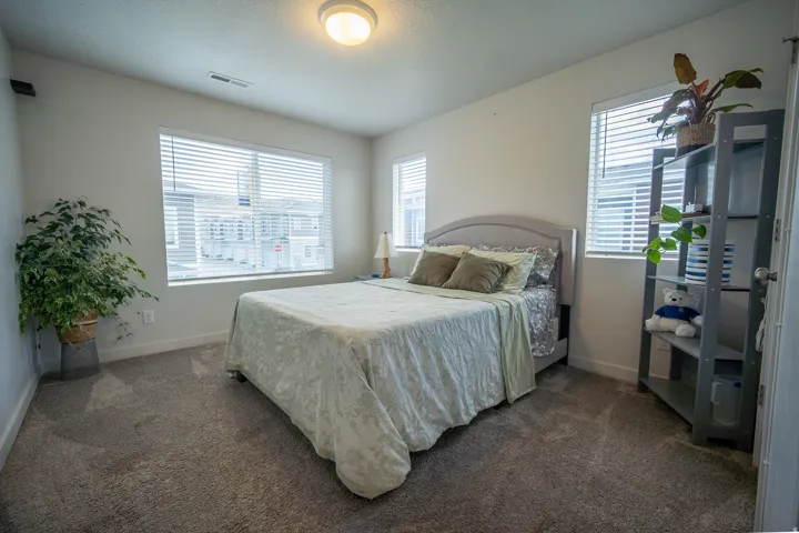 Comfortable secondary bedroom featuring plush carpeting, neutral paint tones, ample natural light, and a functional layout ideal for guests, family, or a home office. Multiple blinds, and an overhead flush-mount light fixture.