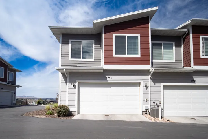 Modern exterior design with a red and gray facade, sloped roofline, attached garage, and multiple windows