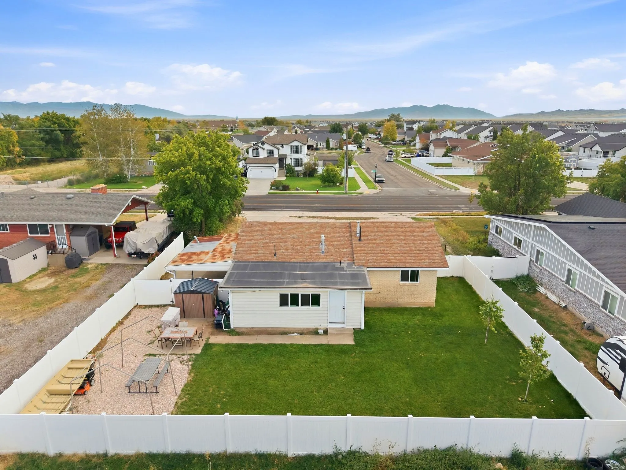 Expansive backyard featuring a manicured lawn, gravel patio area, and white privacy fencing