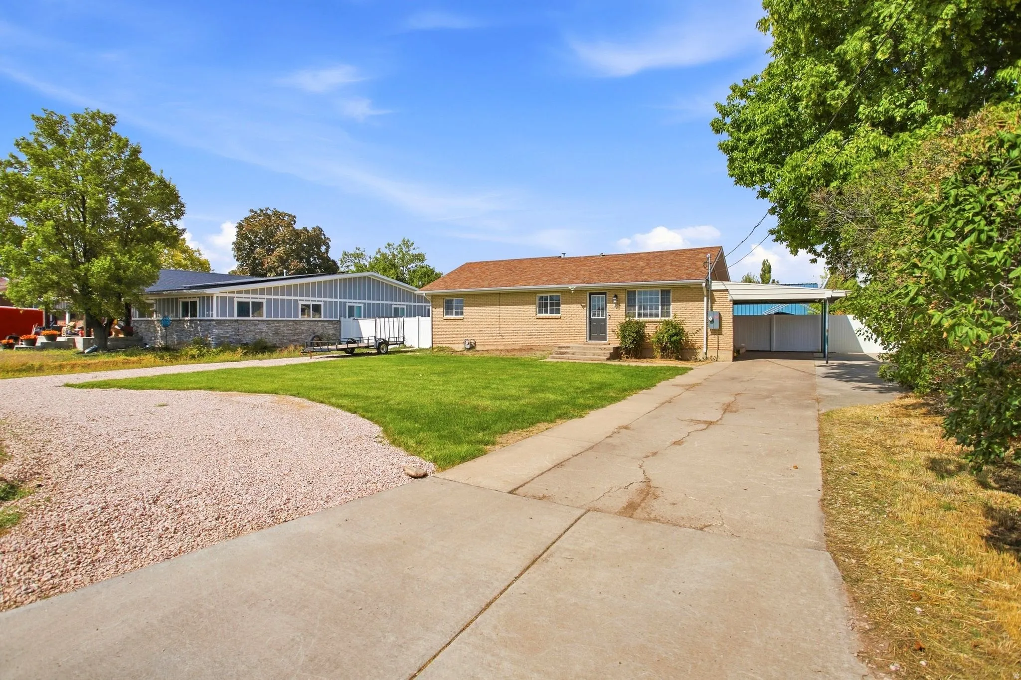 Brick exterior with a covered carport, mature trees, and a concrete driveway
