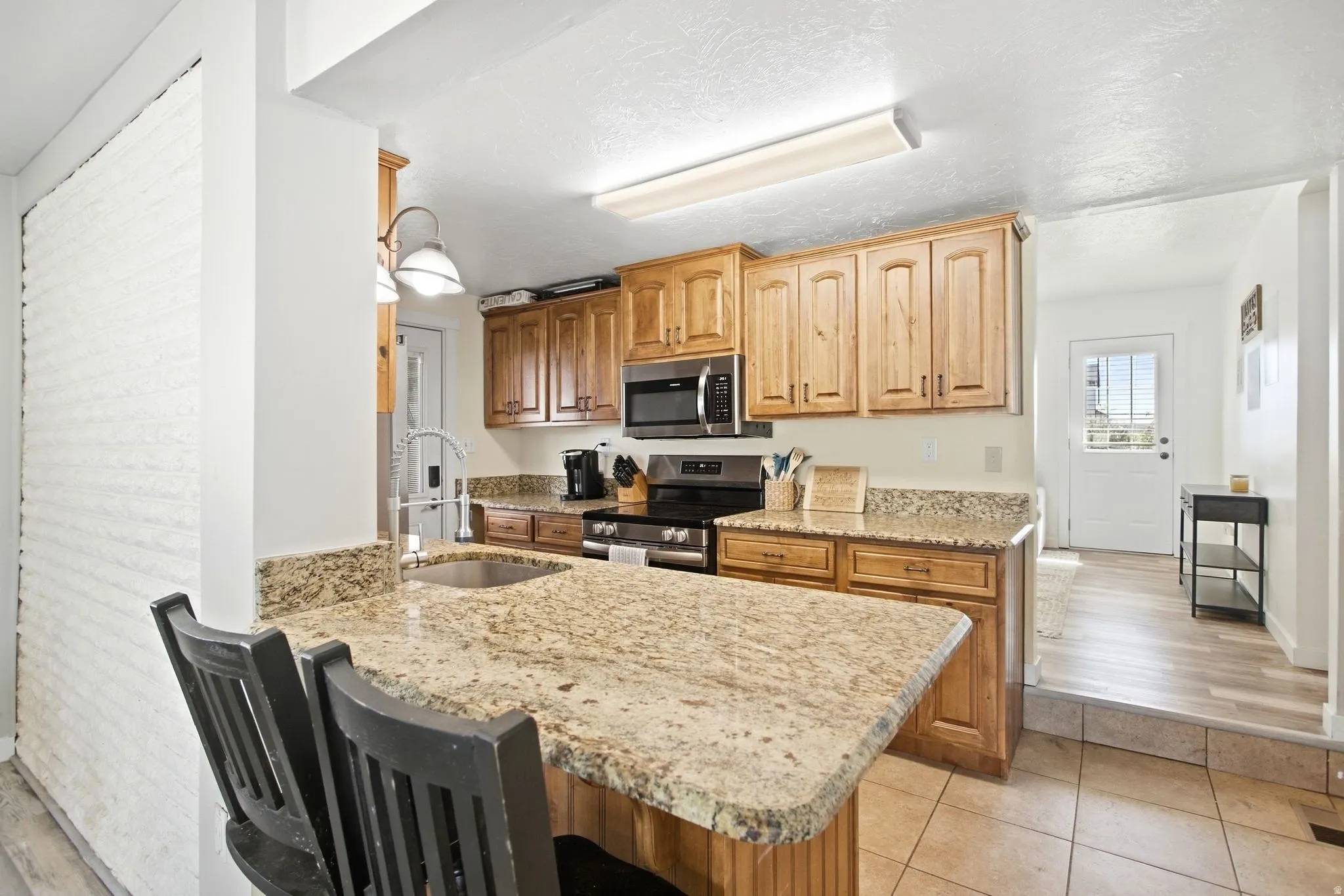 Kitchen featuring wood cabinetry, granite countertops, tile flooring, and stainless steel appliances