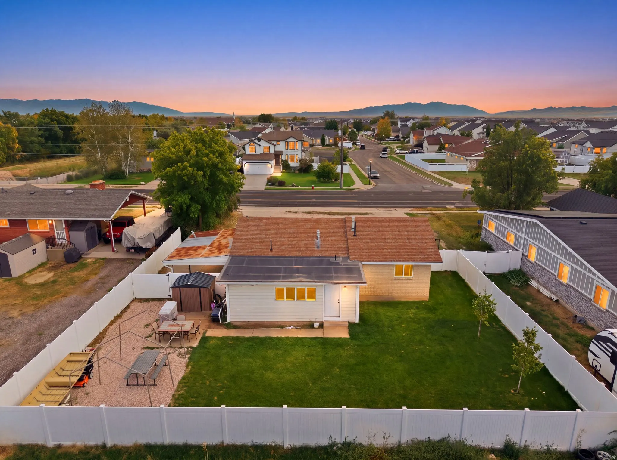 Expansive backyard featuring a manicured lawn, white vinyl fencing, and a gravel patio area