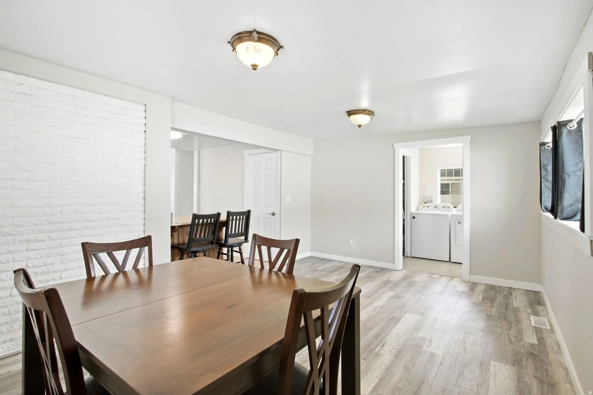 Wood-finish flooring, white brick-style accent wall, and ceiling-mounted light fixtures