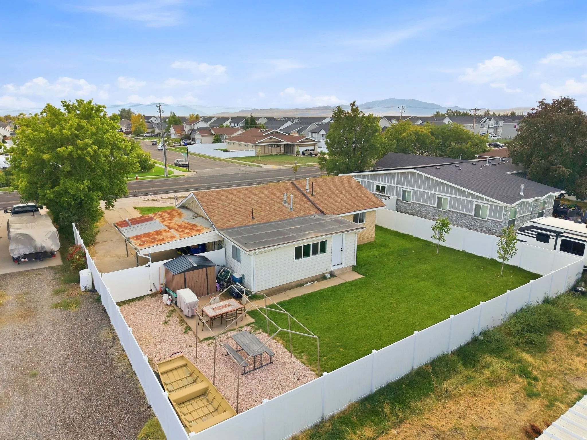 Expansive backyard featuring a manicured lawn, white privacy fencing, and a gravel patio area