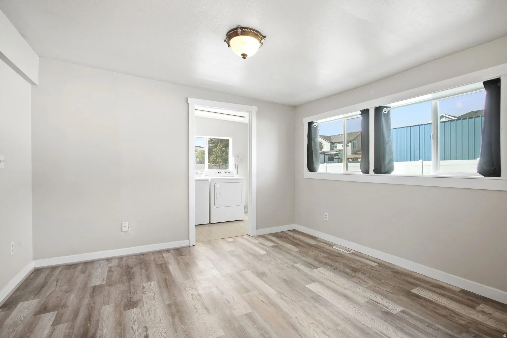 Wood-finish flooring throughout, light neutral wall tones, multi-pane window, and a ceiling-mounted light fixture