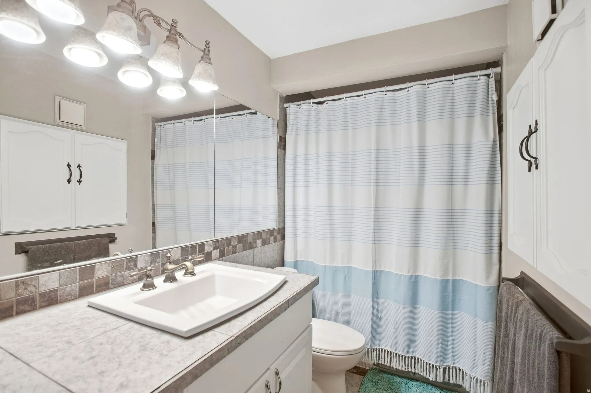 Vanity with integrated sink, mosaic tile backsplash, and overhead lighting fixture