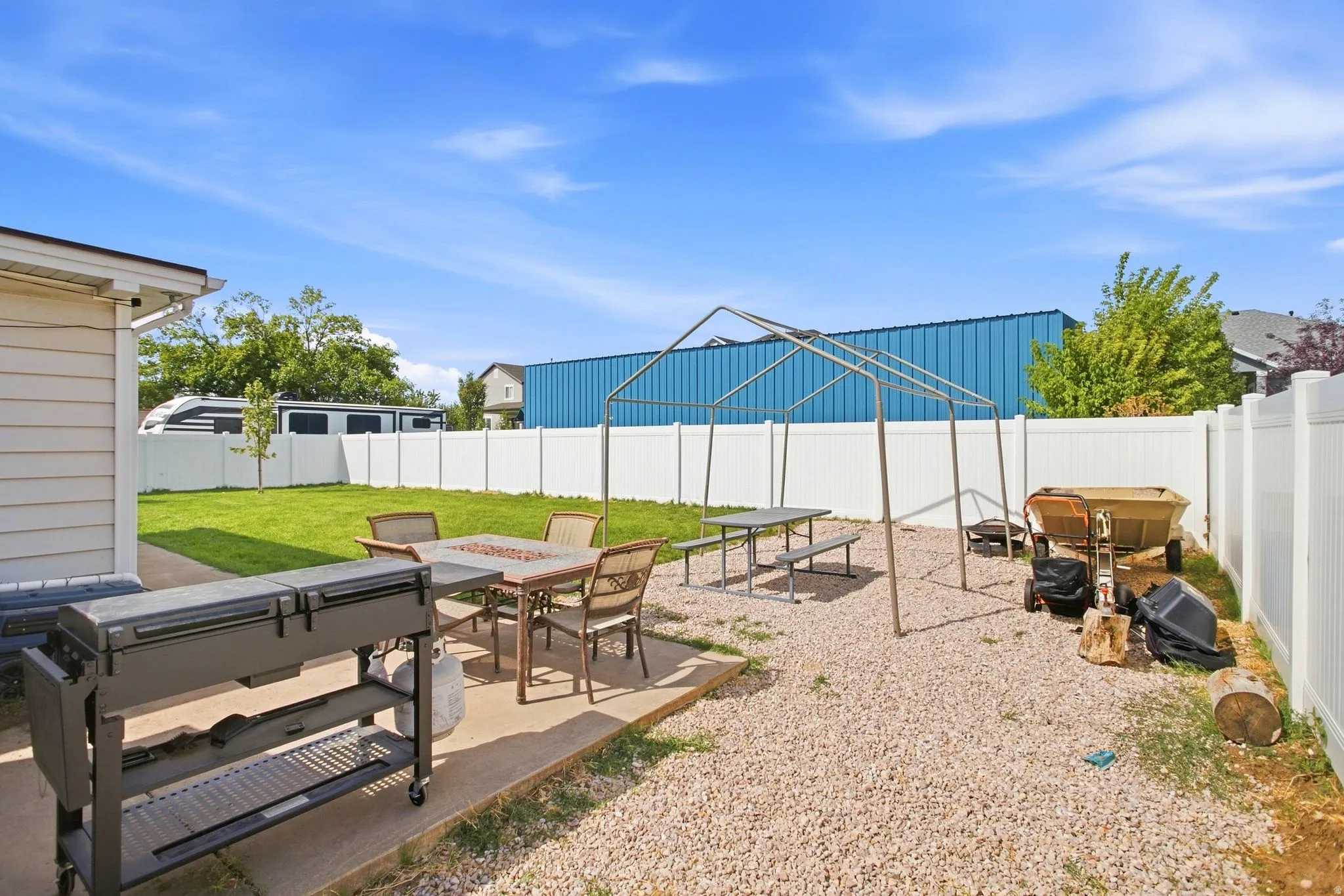 Expansive backyard featuring a concrete patio, gravel area, and a lush lawn, all enclosed by a white privacy fence