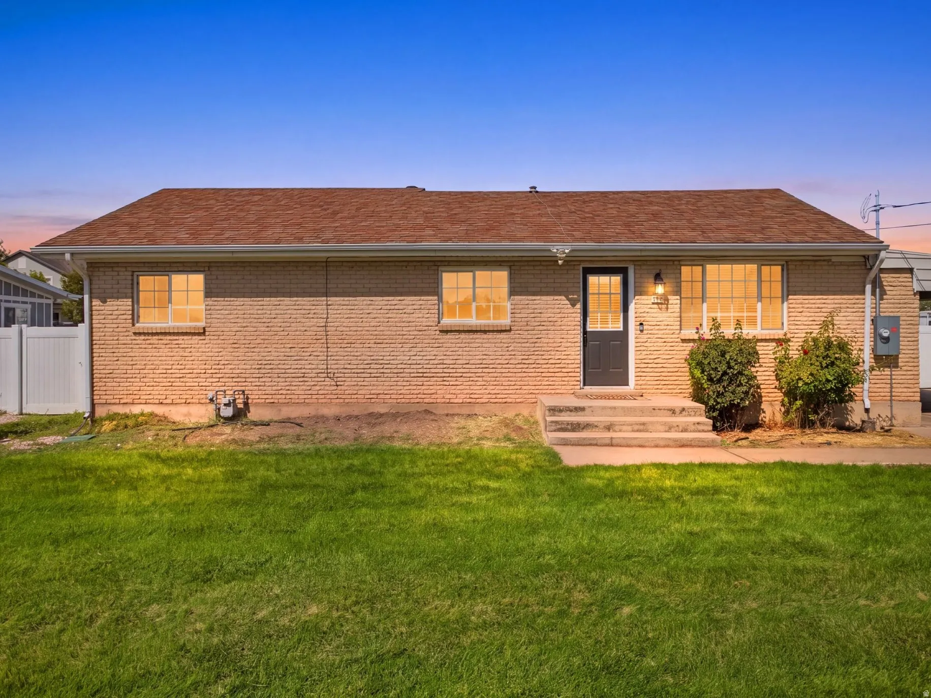 Brick exterior with a brown shingle roof, concrete porch, and established shrubbery