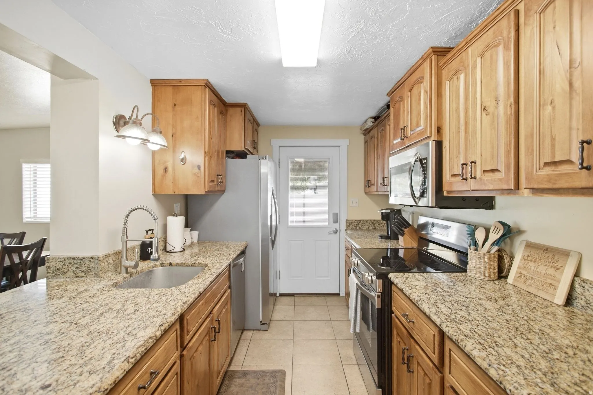 Galley kitchen featuring wood cabinetry, granite-style countertops, stainless steel appliances, a stainless steel sink, and recessed lighting