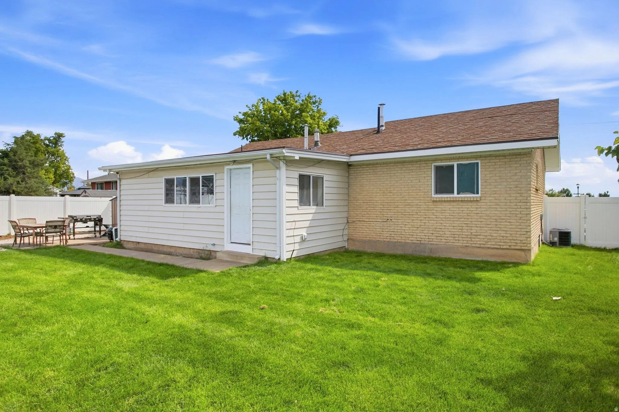 Expansive green lawn, white vinyl fencing, concrete patio, light brick exterior, and white siding