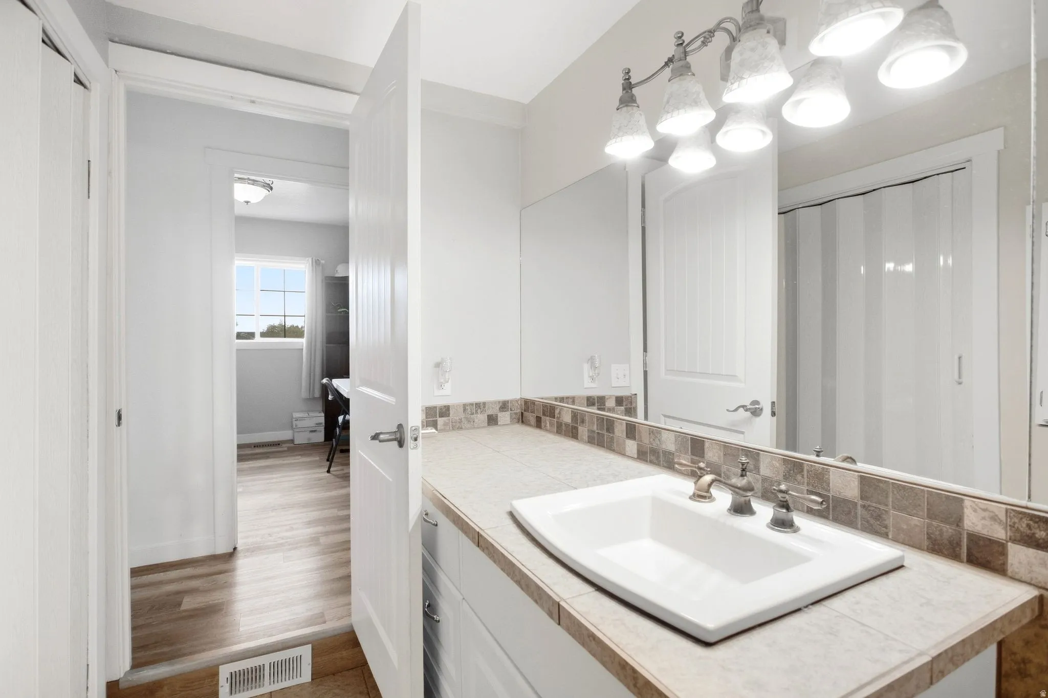 White vanity with a neutral-toned countertop, rectangular undermount sink, and a multi-bulb light fixture