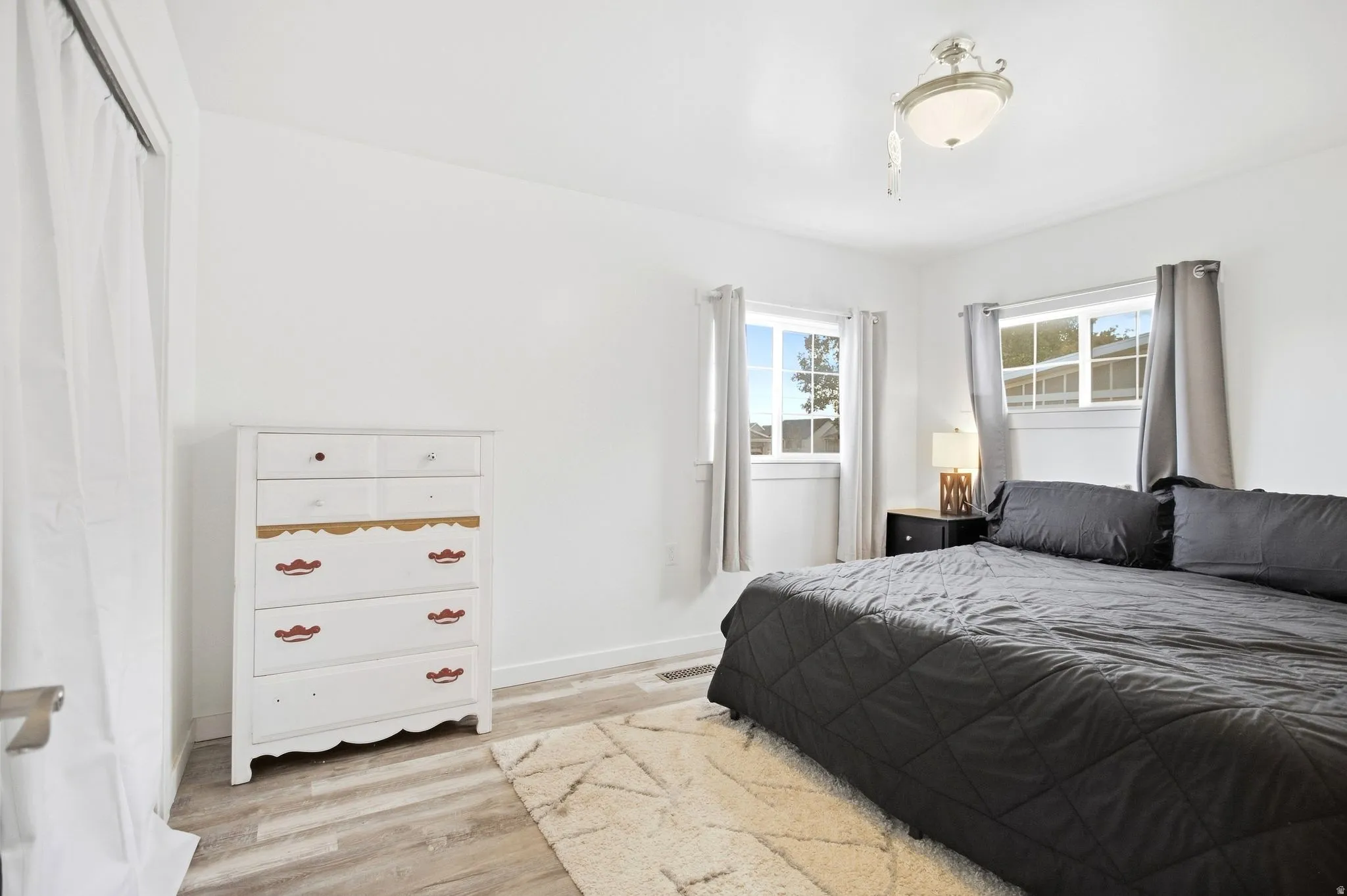 White walls, two windows, wood-finish flooring, and a semi-flush mount ceiling light