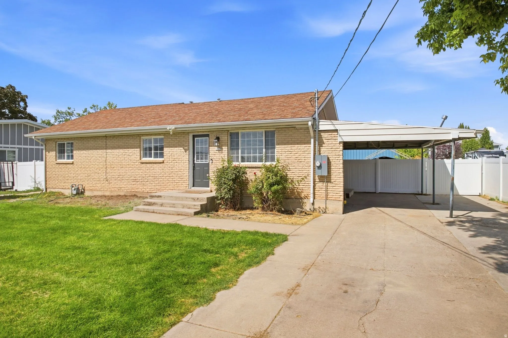 Brick exterior, brown shingle roof, front entry with storm door, covered carport, and fenced yard