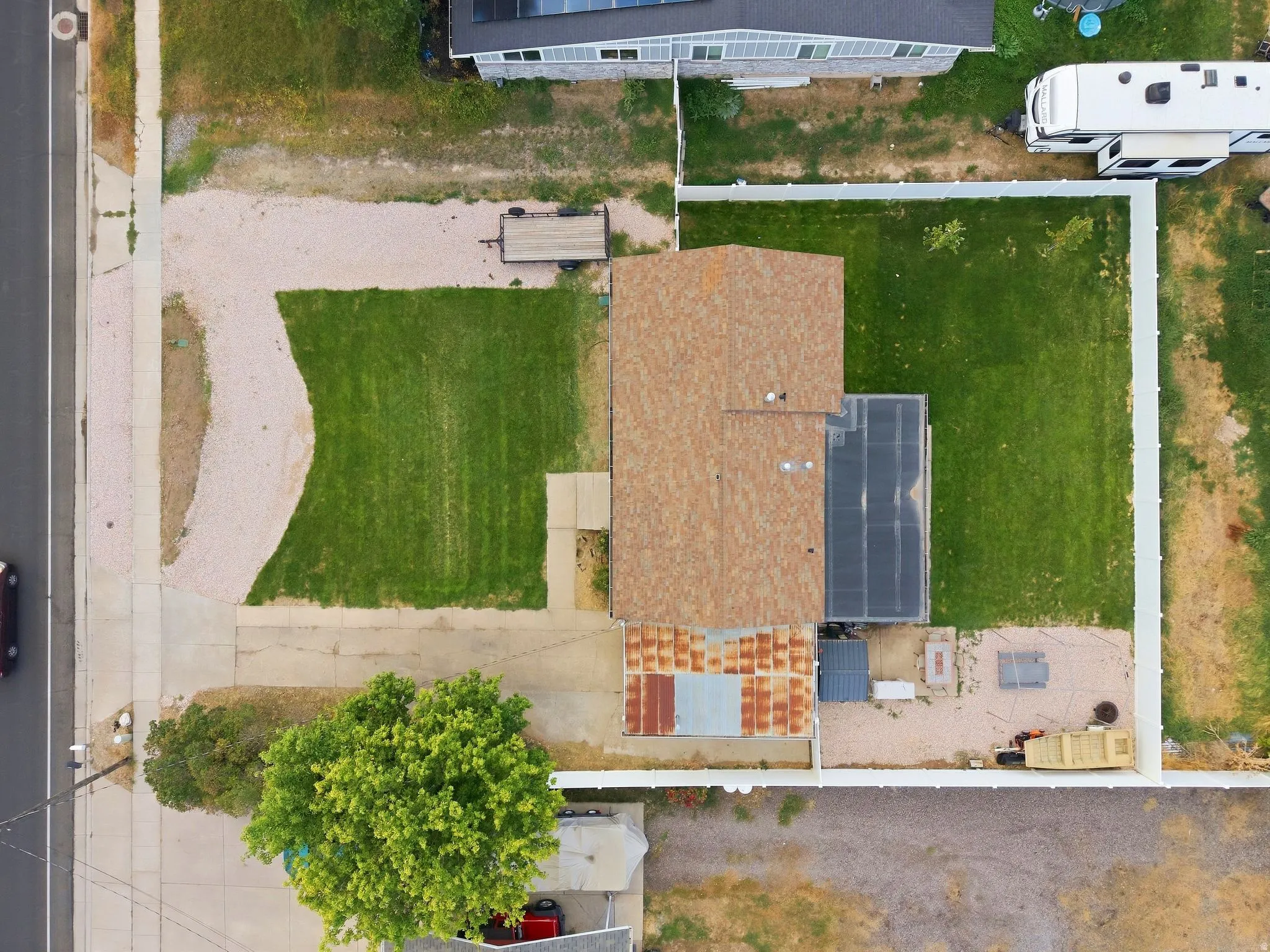 Fenced property with a gravel driveway, a large lawn area, and a brown shingle roof