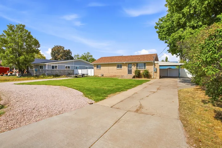 Brick exterior with a covered carport, mature trees, and a concrete driveway