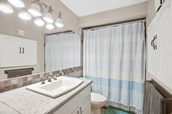 Vanity with integrated sink, mosaic tile backsplash, and overhead lighting fixture