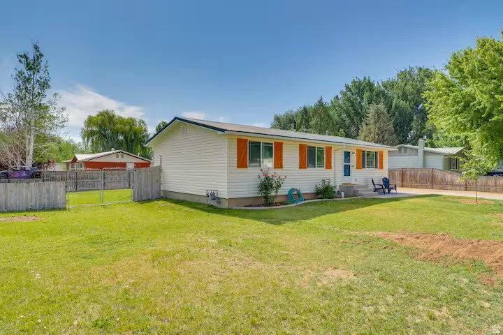 White siding exterior with orange shutters, a concrete patio, a concrete driveway, a front lawn, and a partial wood fence