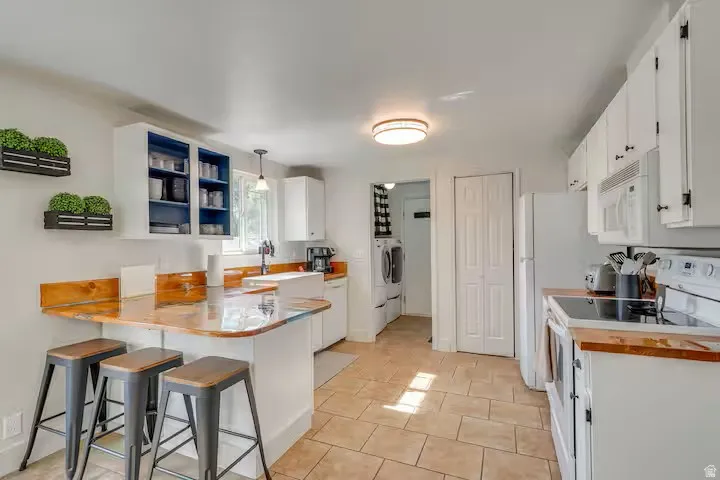 Kitchen featuring white cabinetry, wood-finish countertops, ceramic tile flooring, and an integrated breakfast bar
