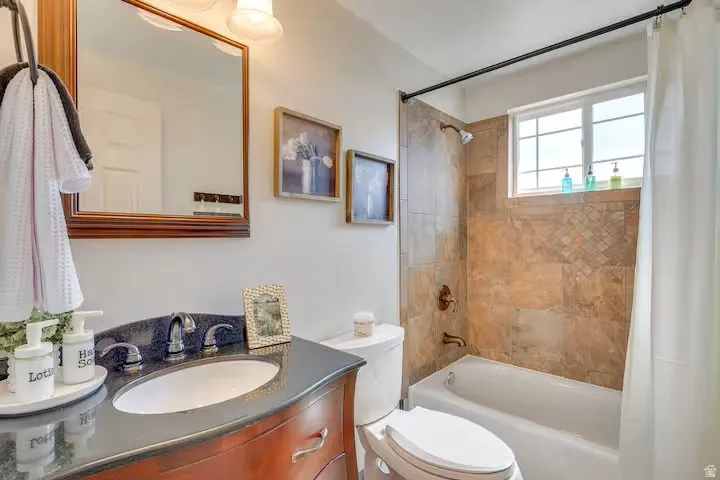Bathroom featuring a vanity with dark countertop, large framed mirror, tiled shower surround, built-in bathtub, and window