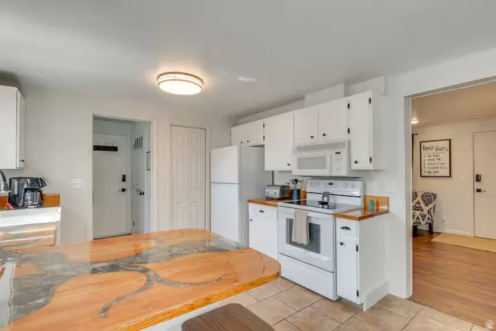 Kitchen featuring white cabinetry, white appliances, tile flooring, wood-finish countertops, and an integrated lighting fixture