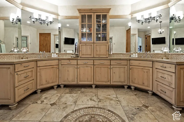 Dual vanities with integrated sinks, extensive wood cabinetry, tile flooring with mosaic inlay, custom lighting fixtures, and large wall-mounted mirrors