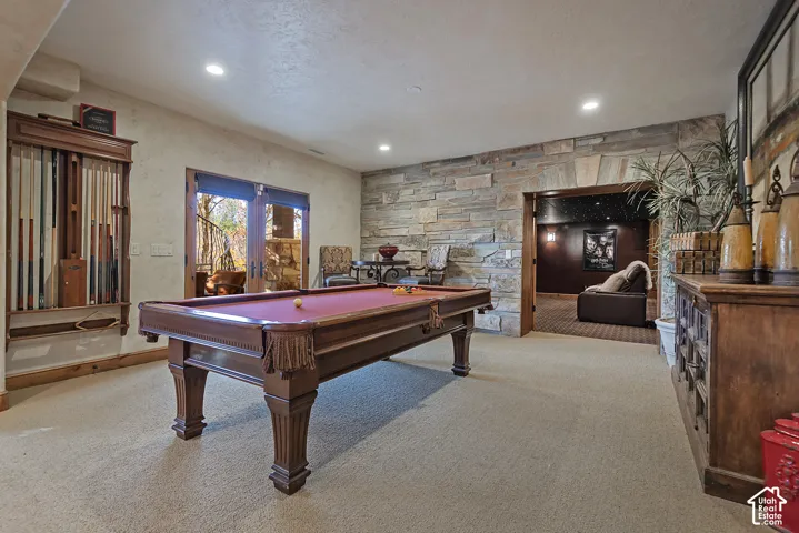Carpeted recreation room featuring a billiards table, stone accent wall, and wood-framed glass doors