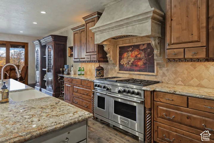 Gourmet kitchen featuring a stainless steel professional-grade range, custom cabinetry, stone countertops, a decorative range hood, and a tile backsplash