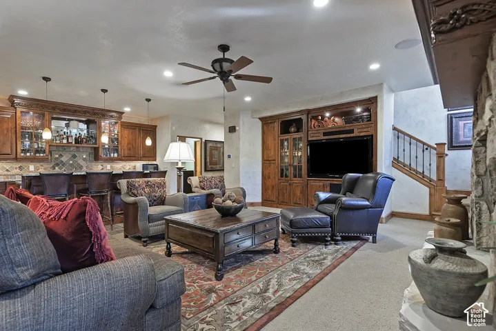 Built-in entertainment center with integrated shelving, ceiling fan with light fixture, recessed lighting, built-in wet bar with pendant lighting, and stone surround fireplace