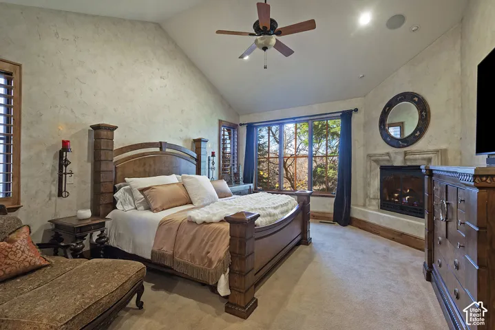 Vaulted ceiling, stone-textured walls, integrated ceiling fan, large window with outdoor scenery, and a built-in fireplace with a stone mantel
