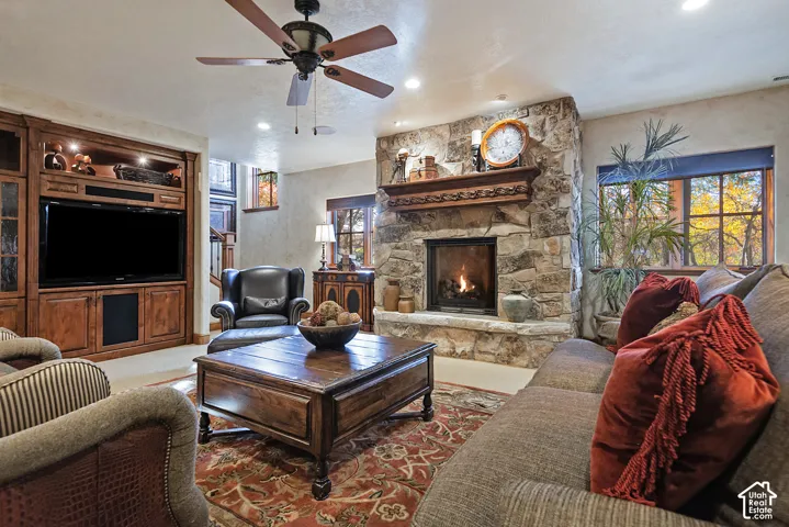 Stone-faced fireplace with a carved wood mantel, wood-finish media built-in, and ceiling fan with lighting