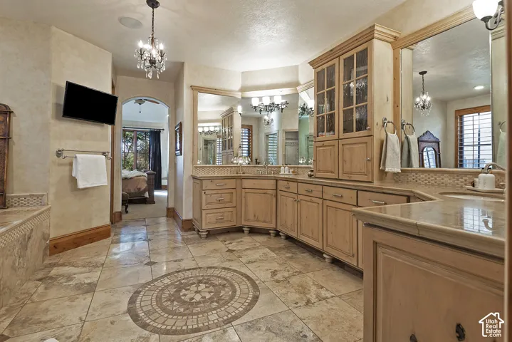Tile flooring with a decorative mosaic inlay, extensive wood cabinetry, integrated dual vanities, large wall-mounted mirrors, and an arched doorway
