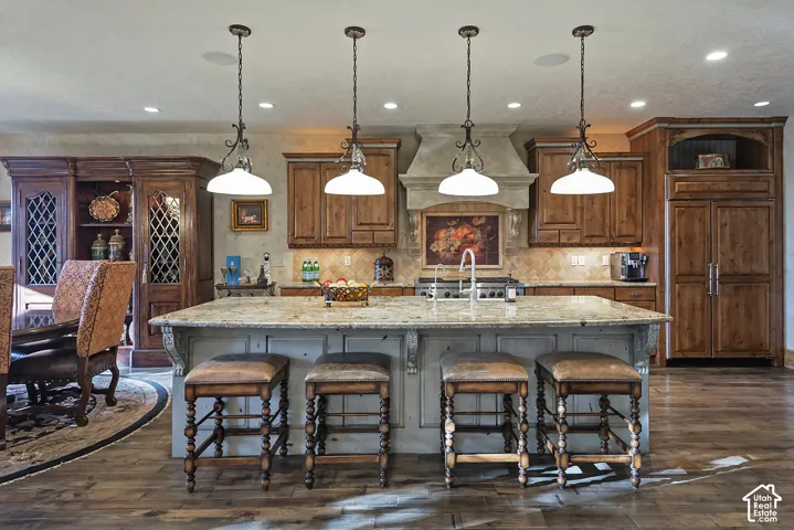 Custom cabinetry, stone countertops, wood-finish flooring, built-in refrigerator, and integrated range hood