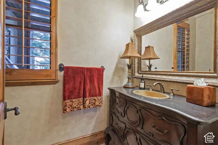 Custom wood plantation shutters, ornate vanity with integrated sink, framed mirror, wall-mounted light fixture, and floor-level wood trim