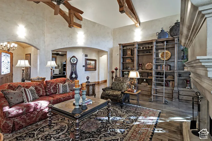 Vaulted ceiling with exposed wood beams, built-in shelving with a rolling ladder, wood-finish flooring, arched doorways, and a stone fireplace surround