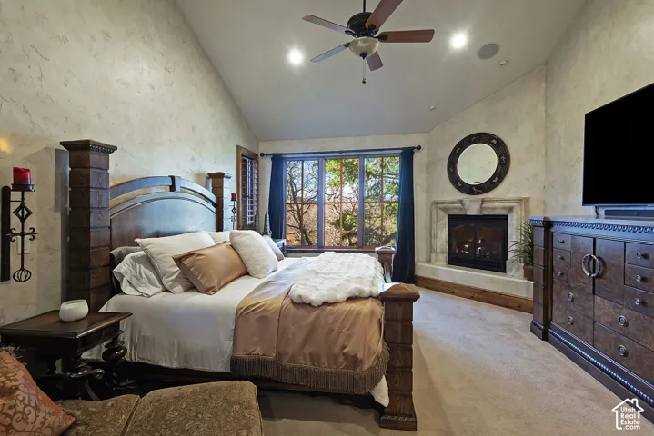 Vaulted ceiling with ceiling fan, recessed lighting, large window with dark drapes, corner fireplace with stone surround, and textured wall finish
