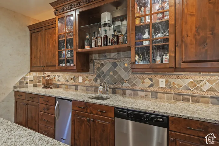 Custom wood cabinetry featuring glass-front doors, a granite countertop, and a built-in stainless steel dishwasher