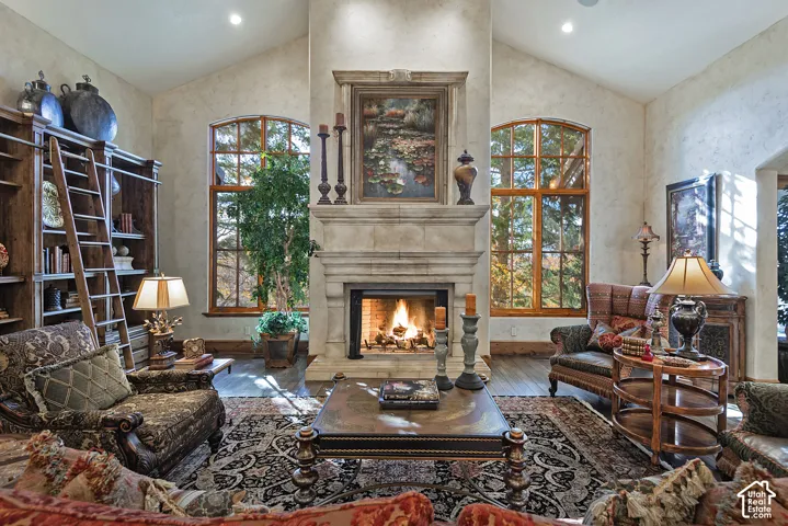 Vaulted ceilings with recessed lighting, stone-clad fireplace with mantel, arched windows with wood frames, wood-finish flooring, and built-in shelving with ladder