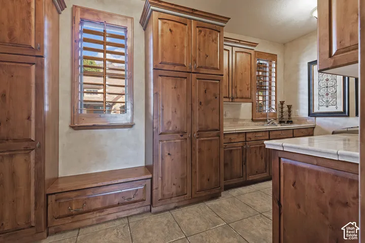 Built-in cabinetry with wood finishes, louvered window shutters, recessed lighting, tile flooring, and light-toned countertops