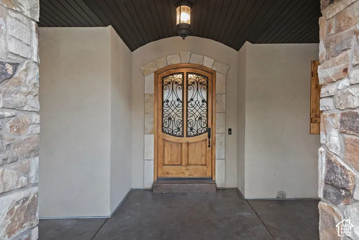 Arch-top wood entry door with ornate wrought iron detailing, stone archway surround, and a coordinating stone veneer column