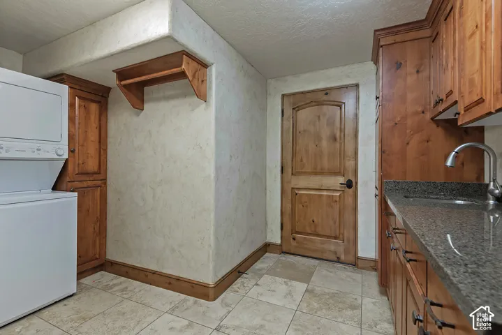 Travertine-style tile flooring, wood-finish cabinetry, built-in utility sink, and stone-finish countertop