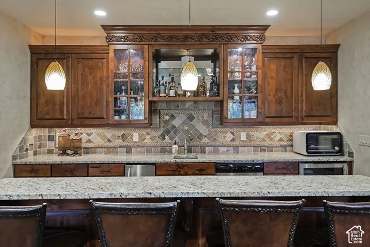 Built-in bar featuring wood cabinetry, integrated lighting, granite-finish countertops, and a tiled backsplash